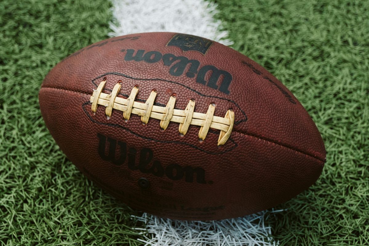 A brown leather football resting on a white yard line on green artificial turf