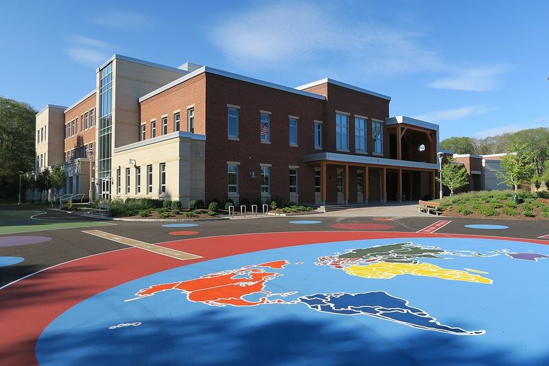 West Parish Elementary School in Gloucester, a three story brick and stone building with a covered entrance, seen across a playground painted with a world map