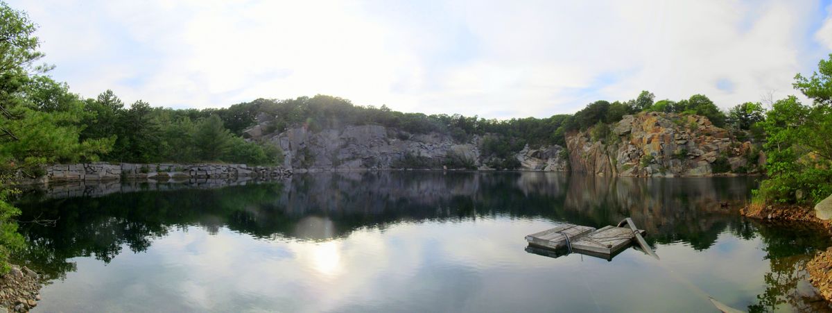 Panorama of Flat Ledge Quarry ringed by granite ledges and trees, with a floating pump intake on the water