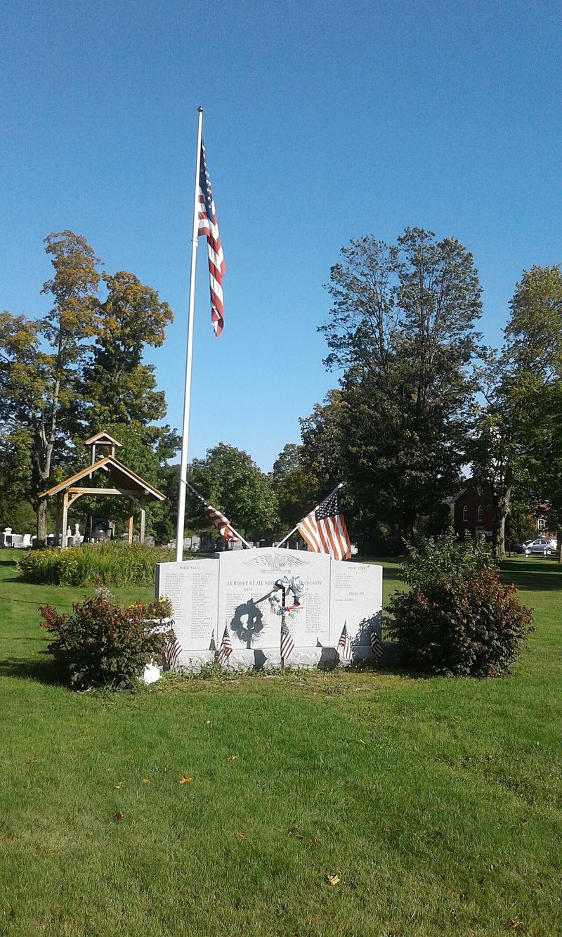 A veterans memorial stone and American flag on a town green